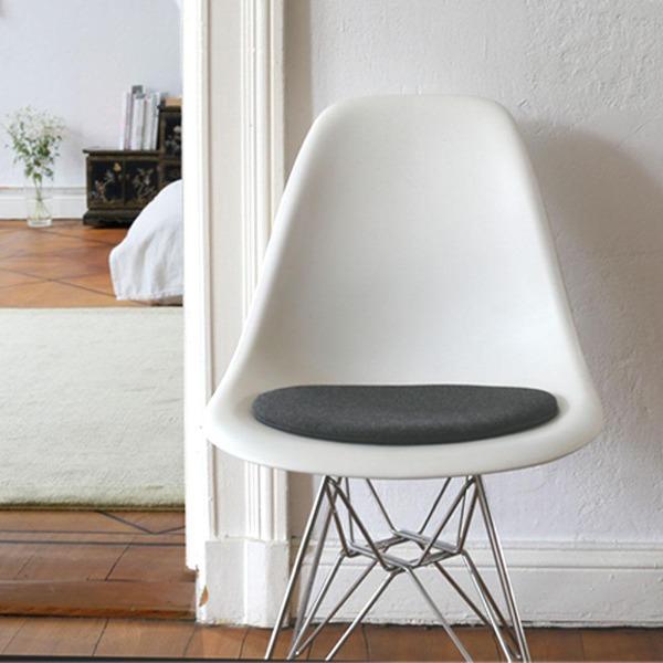 Das foto zeigt einen weissen eames plastic side chair dsr auf dem eine runde sitzauflage der firma discus liegt. Die farbe der sitzauflage ist anthrazit meliert. Der stuhl steht in einem wohnzimmer an der wand.