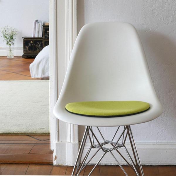 Das foto zeigt einen weissen eames plastic side chair dsr auf dem eine runde sitzauflage der firma discus liegt. Die farbe der sitzauflage ist zitronengelb mit einem leichtem grünstich. Der stuhl steht in einem wohnzimmer an der wand.