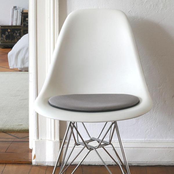 Das foto zeigt einen weissen eames plastic side chair dsr auf dem eine runde sitzauflage der firma discus liegt. Die farbe der sitzauflage ist grau meliert. Der stuhl steht in einem wohnzimmer an der wand.