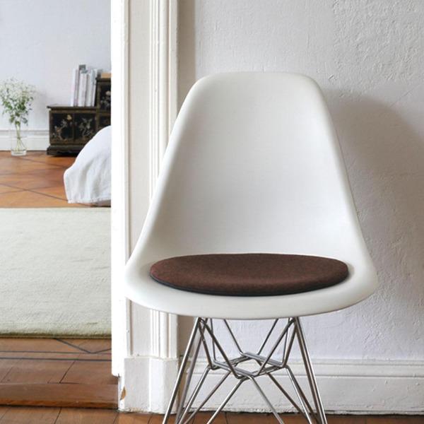 Das foto zeigt einen weissen eames plastic side chair dsr auf dem eine runde sitzauflage der firma discus liegt. Die farbe der sitzauflage ist bordeaux meliert. Der stuhl steht in einem wohnzimmer an der wand.
