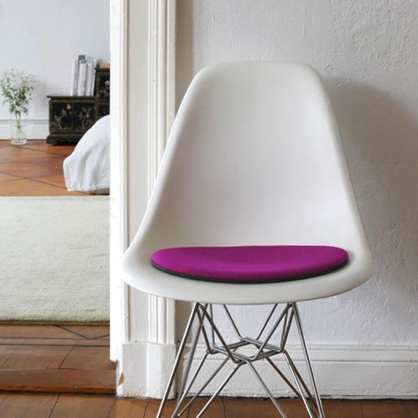 Das foto zeigt einen weissen eames plastic side chair dsr auf dem eine runde sitzauflage der firma discus liegt. Die farbe der sitzauflage ist magenta meliert. Der stuhl steht in einem wohnzimmer an der wand.