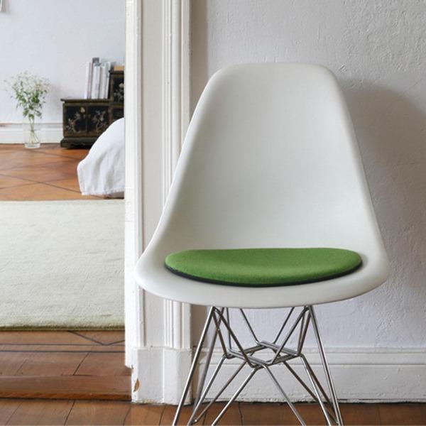 Das foto zeigt einen weissen eames plastic side chair dsr auf dem eine runde sitzauflage der firma discus liegt. Die farbe der sitzauflage ist hellgrün meliert. Der stuhl steht in einem wohnzimmer an der wand.