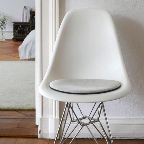 Das foto zeigt einen weissen eames plastic side chair dsr auf dem eine runde sitzauflage der firma discus liegt. Die farbe der sitzauflage ist weiss/hellgrau meliert. Der stuhl steht in einem wohnzimmer an der wand.