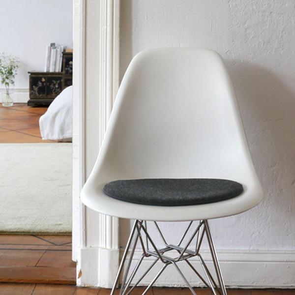 Das foto zeigt einen weissen eames plastic side chair dsr auf dem eine runde sitzauflage der firma discus liegt. Die farbe der sitzauflage ist anthrazit meliert. Der stuhl steht in einem wohnzimmer an der wand.
