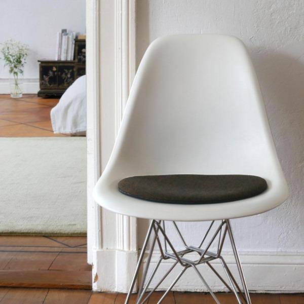 Das foto zeigt einen weissen eames plastic side chair dsr auf dem eine runde sitzauflage der firma discus liegt. Die farbe der sitzauflage ist braun-schwarz meliert. Der stuhl steht in einem wohnzimmer an der wand.