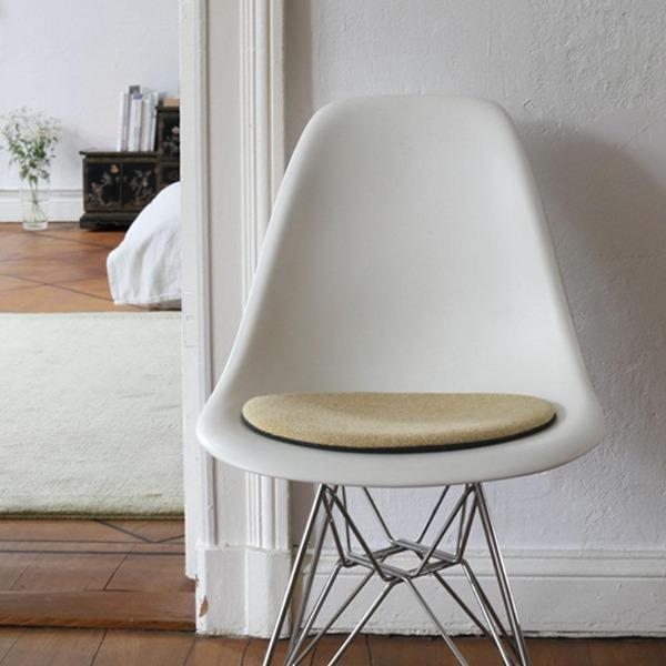 Das foto zeigt einen weissen eames plastic side chair dsr auf dem eine runde sitzauflage der firma discus liegt. Die farbe der sitzauflage ist weiss-senfgelb meliert. Der stuhl steht in einem wohnzimmer an der wand.
