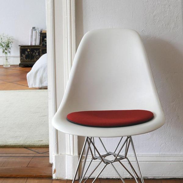 Das foto zeigt einen weissen eames plastic side chair dsr auf dem eine runde sitzauflage der firma discus liegt. Die farbe der sitzauflage ist bordeaux. Der stuhl steht in einem wohnzimmer an der wand.