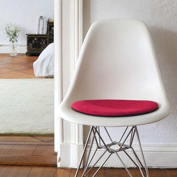 Das foto zeigt einen weissen eames plastic side chair dsr auf dem eine runde sitzauflage der firma discus liegt. Die farbe der sitzauflage ist pink-orange meliert. Der stuhl steht in einem wohnzimmer an der wand.