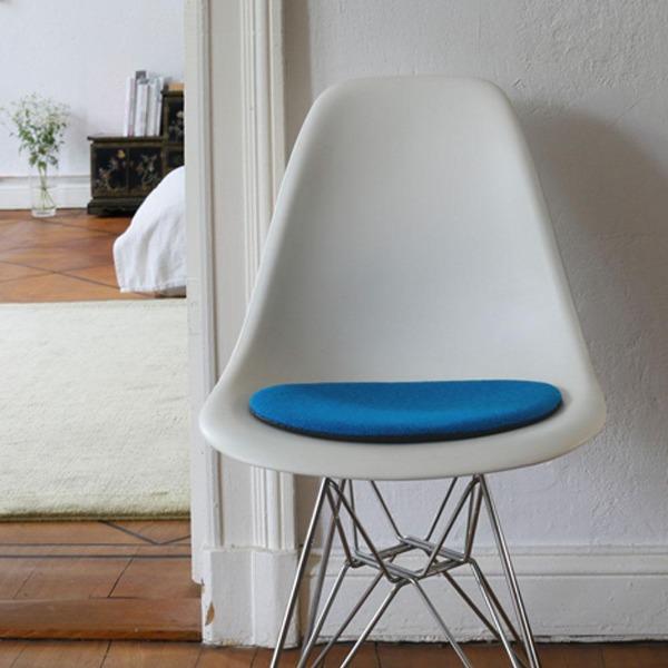 Das foto zeigt einen weissen eames plastic side chair dsr auf dem eine runde sitzauflage der firma discus liegt. Die farbe der sitzauflage ist blau-tuerkis meliert. Der stuhl steht in einem wohnzimmer an der wand.