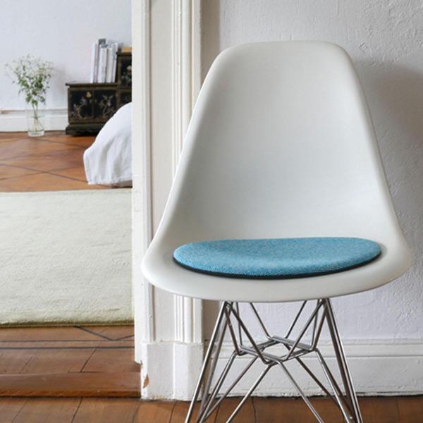 Das foto zeigt einen weissen eames plastic side chair dsr auf dem eine runde sitzauflage der firma discus liegt. Die farbe der sitzauflage ist weiss-tuerkis meliert. Der stuhl steht in einem wohnzimmer an der wand.