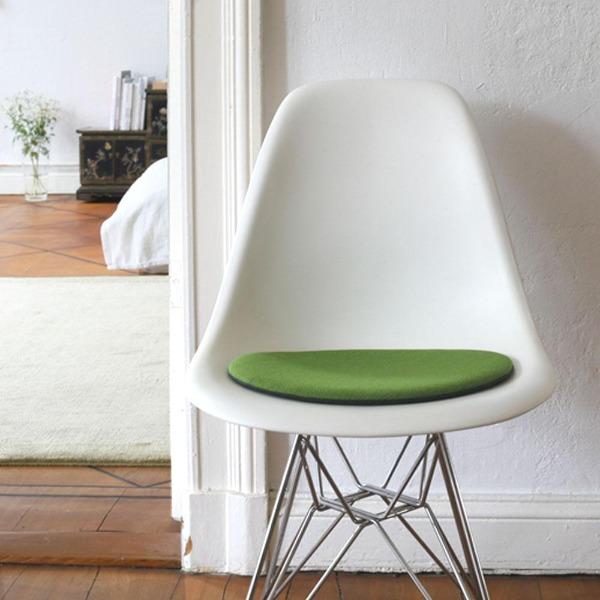Das foto zeigt einen weissen eames plastic side chair dsr auf dem eine runde sitzauflage der firma discus liegt. Die farbe der sitzauflage ist hellgrün-anthrazit meliert. Der stuhl steht in einem wohnzimmer an der wand.