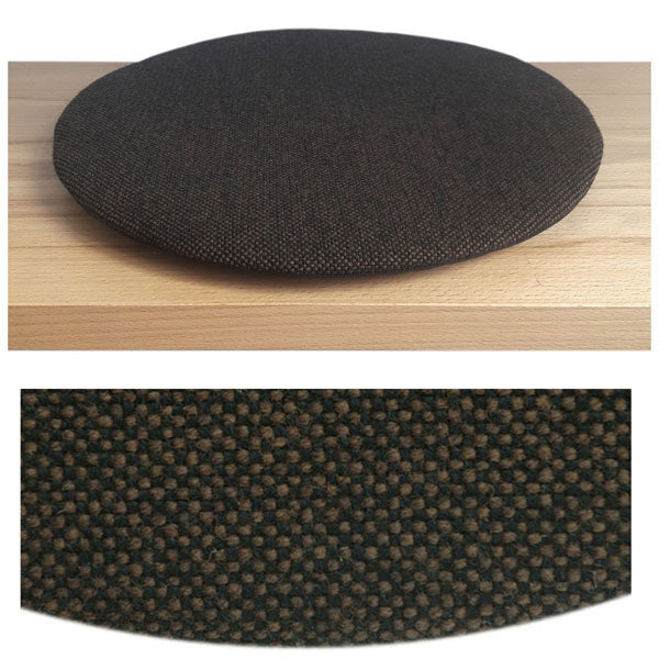 Das foto zeigt eine runde sitzauflage der firma discus. Das sitzkissen verjüngt sich zum rand hin und bildet eine schattenfuge aus. Die farbe der sitzauflage ist braun-schwarz meliert.