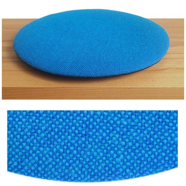 Das foto zeigt eine runde sitzauflage der firma discus. Das sitzkissen verjüngt sich zum rand hin und bildet eine schattenfuge aus. Die farbe der sitzauflage ist blau-tuerkis meliert.